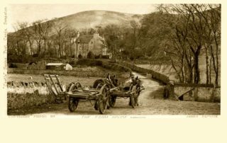Image shows an old photograph taken by photographer James Patrick during the 1800's of two horses and carts being led up to Swanston Farmhouse surrounded by some trees and part of Caerketton Hill in the background.