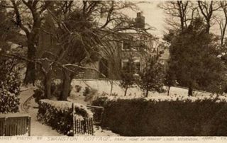 Image shows a very old postcard of a black and white photograph taken by James Patrick in the 1800's of Swanston Cottage, the big white house which was the early home of Robert Louis Stevenson and his family during holidays. There is snow lying on the ground and the house is partly hidden by a large tree.