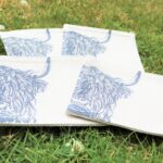 Photograph shows 4 cream linen coasters with highland cow heads printed on them, displayed on a grass background.