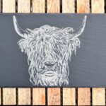 Photograph shows a slate table board with the head of a Highland Cow etched on it